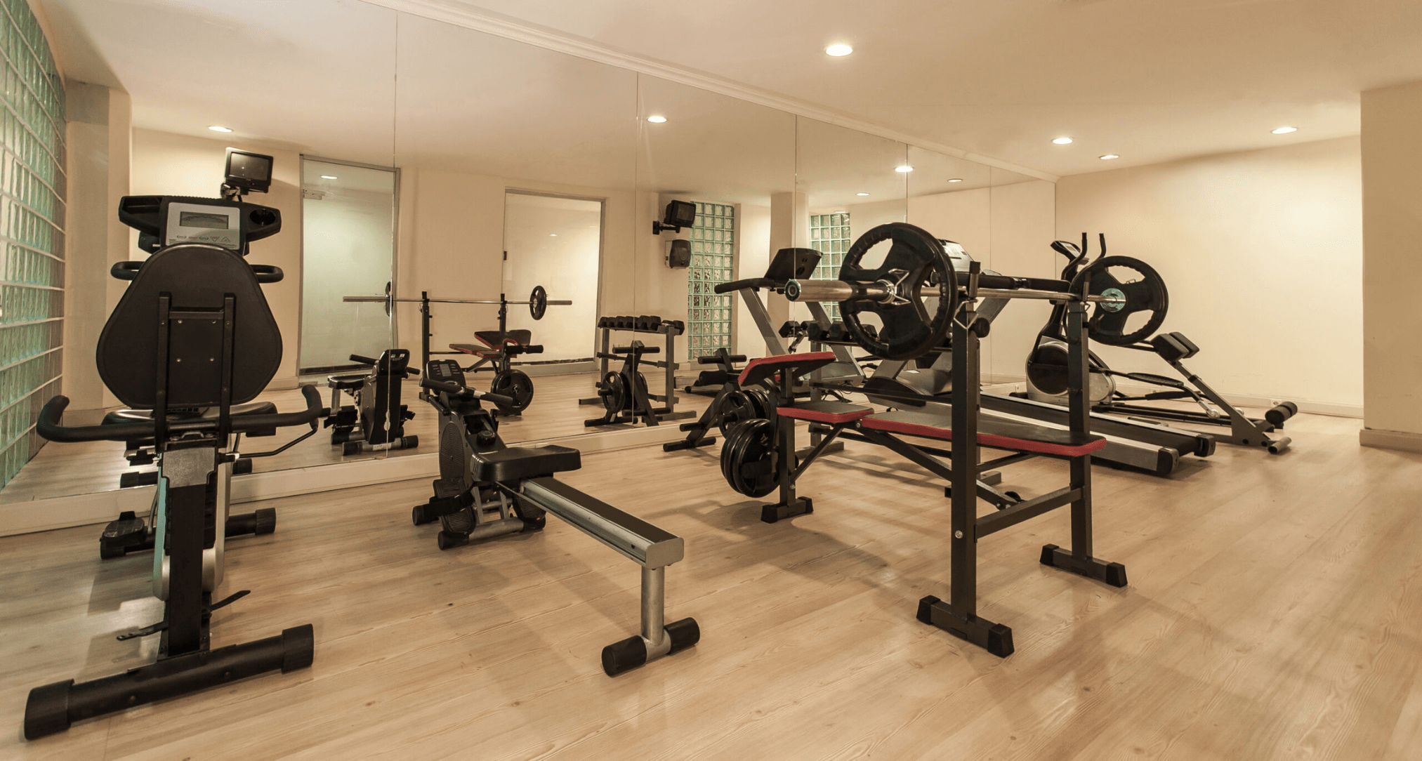Image of various cardio equipment and a weight bench in a room.