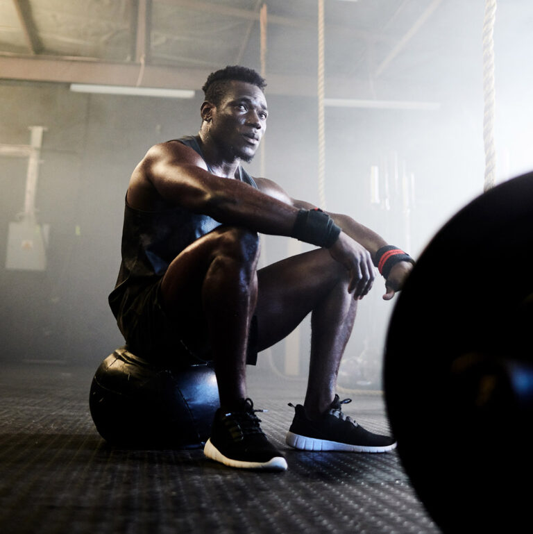 Dark skinned man sitting in gym on a ball thinking about lifting