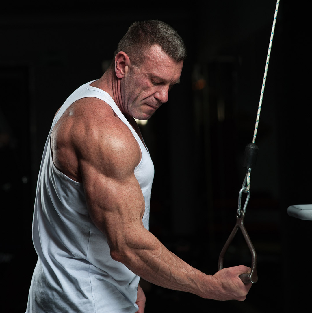 Mature muscular man in white tank top doing a cable single arm cable reverse grip press down