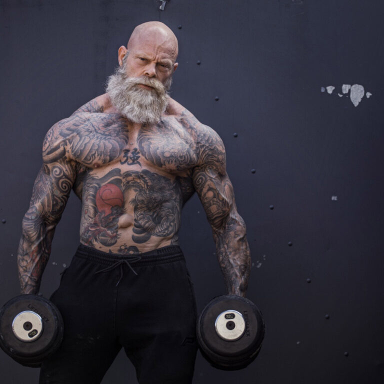 Very muscular and tattooed senior man holding dumbbells.