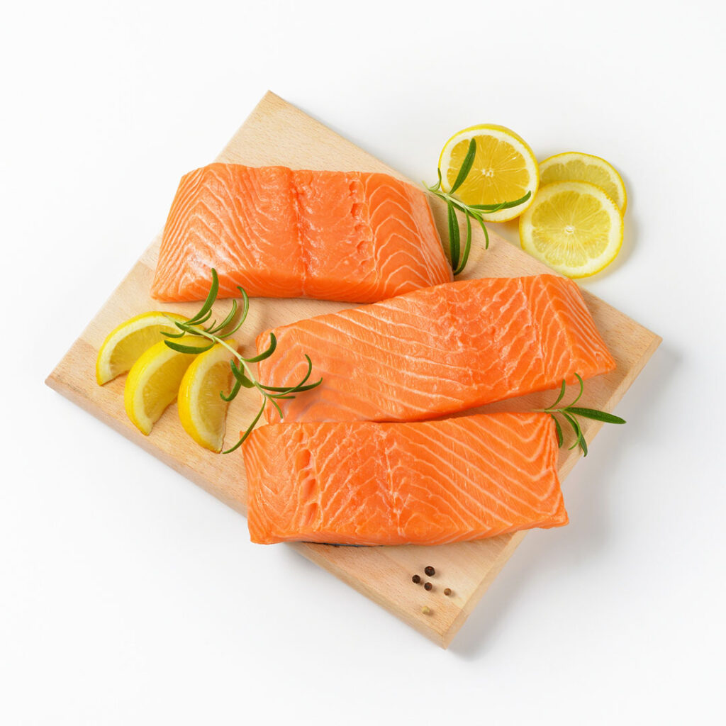 Fresh salmon fillets on a cutting board with lemon slices