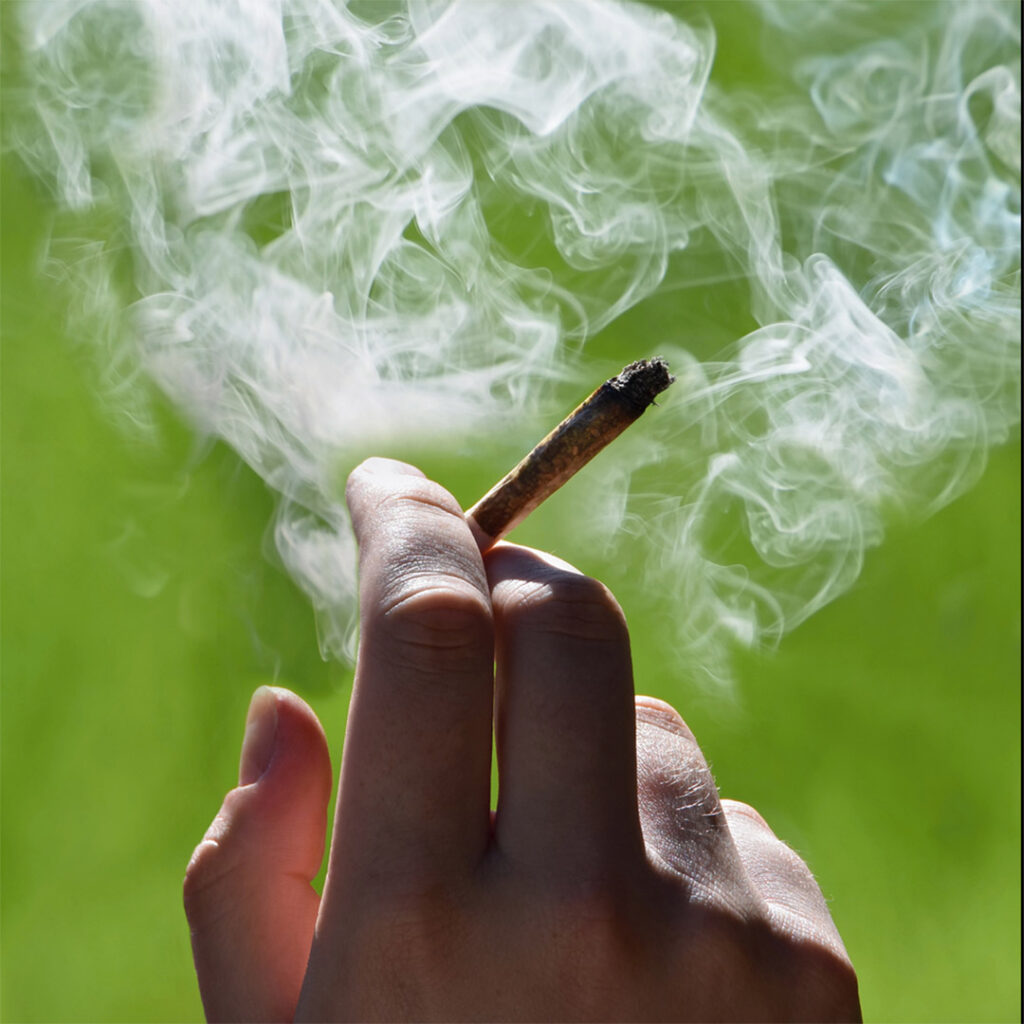 Hand holding a weed cigarette and surrounded by smoke