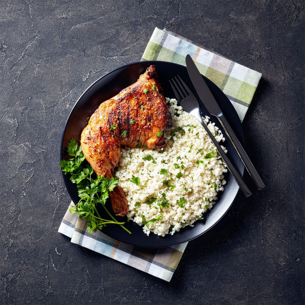Image of a roasted chicken leg quarter with cauliflower rice on a plate