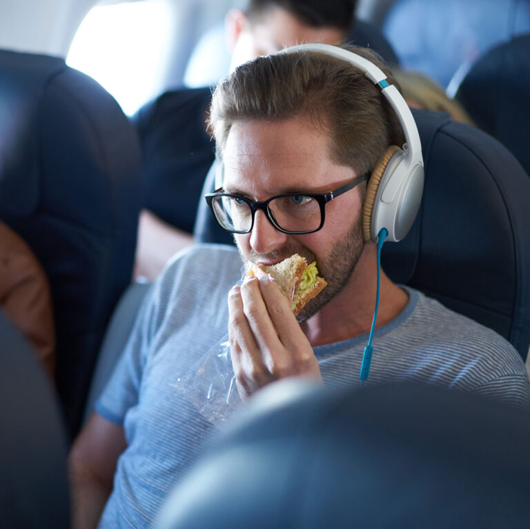 Man wearing headphones sitting in seat on plane munching on a sandwich