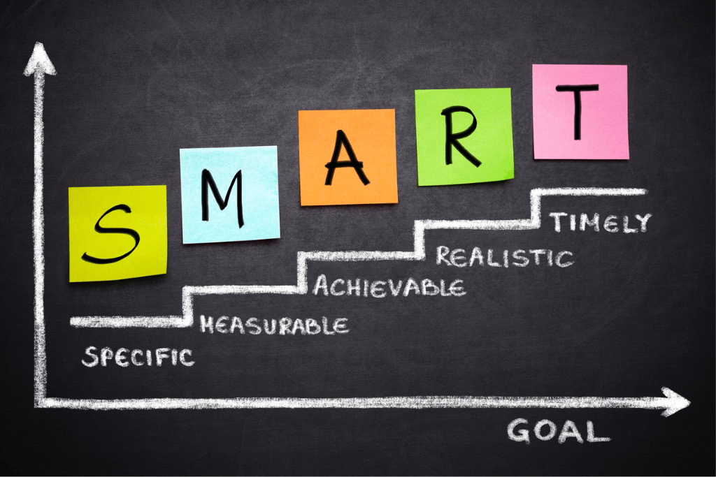 Illustration showing SMART goals acronym spelled in multi-colored squares on blackboard to represent specific, measurable, achievable, realistic, and timely goals.