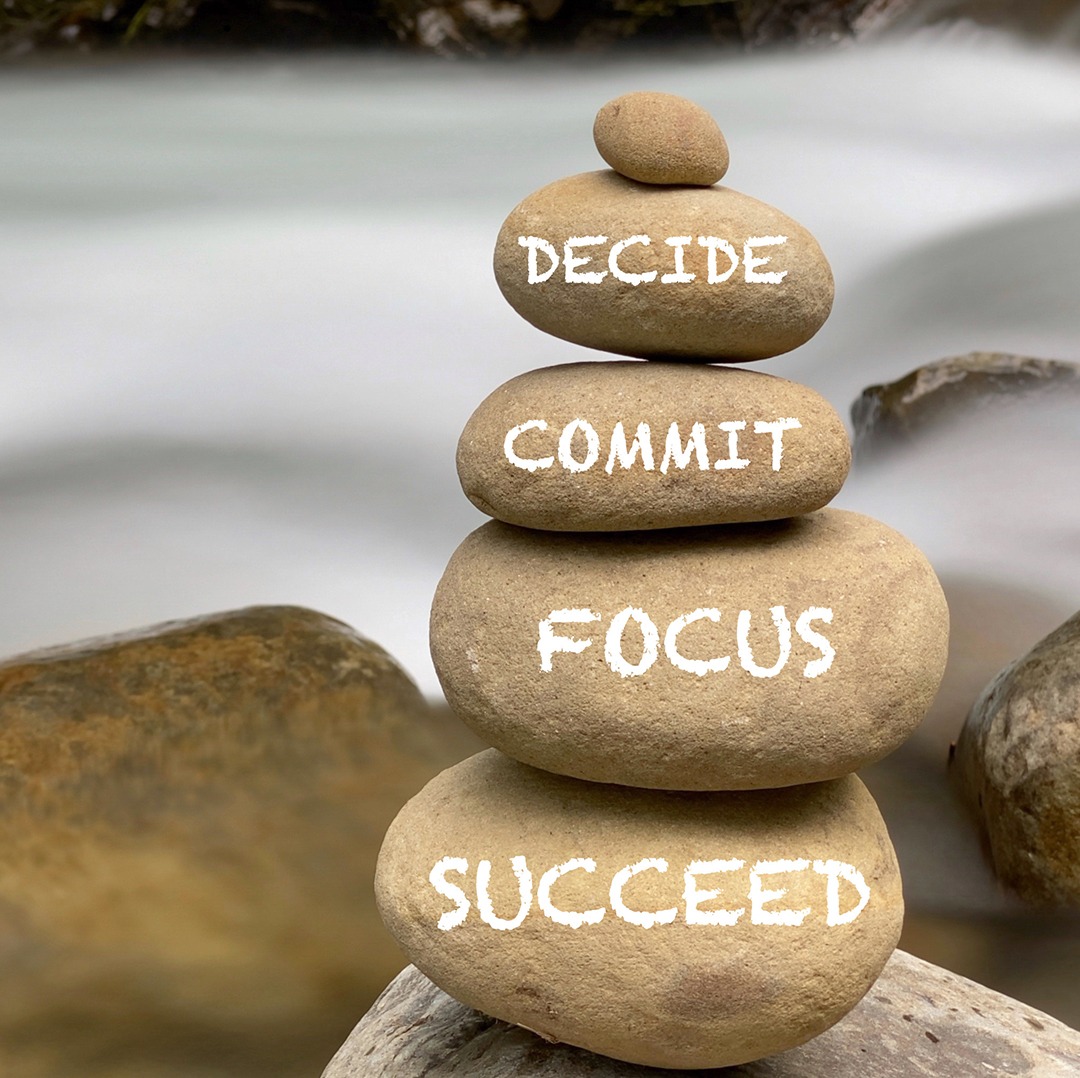 A stack of rocks with words in white written on each reading: decide, commit, focus, and succeed